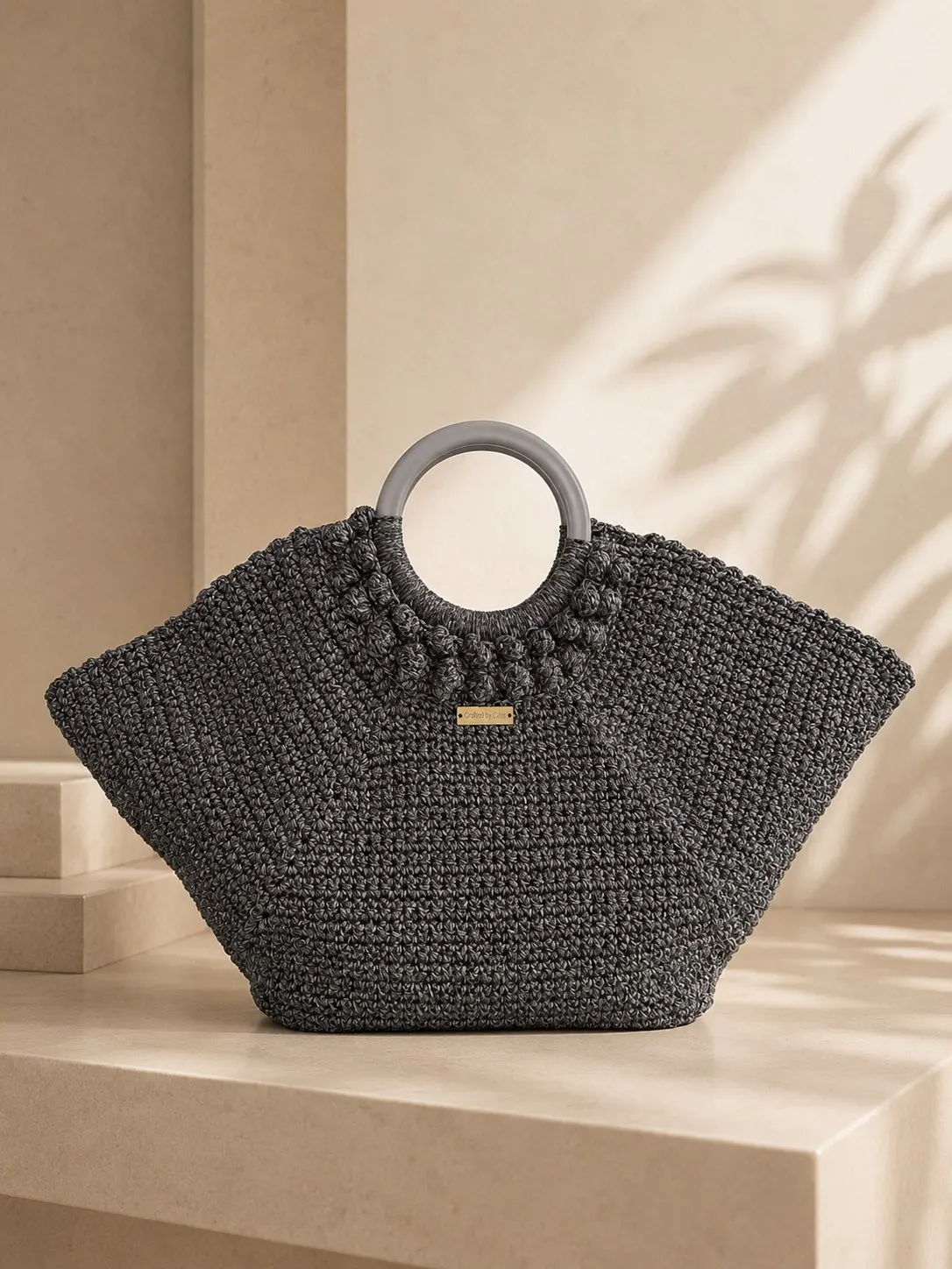 Charcoal crochet basket bag with a wide fan shape and round grey ring handles