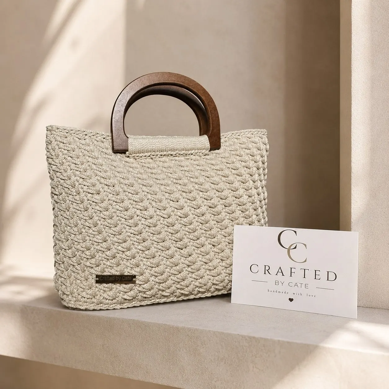 Ivory crochet handbag in a shell-textured stitch with dark curved wooden handles, beside a Crafted By Cate card