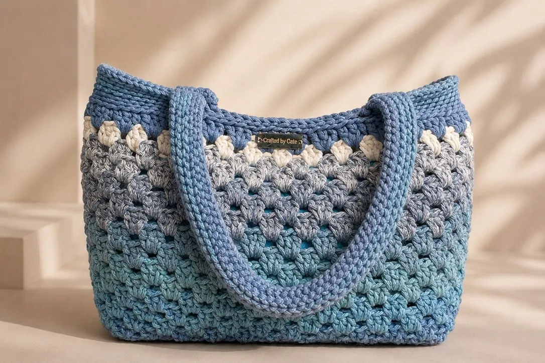 Crochet shoulder tote worked in a gradient from denim blue through grey to sea green, with a row of cream detail and thick rolled handles