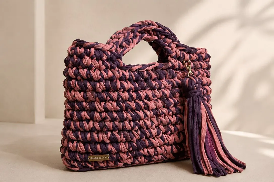 Chunky crochet handbag in marled plum and rose yarn, with a cut-out top handle and a long matching tassel charm