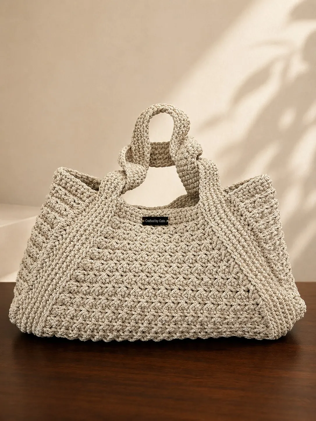Large oatmeal crochet tote in a thick dense stitch with knotted loop handles, on a dark wooden table